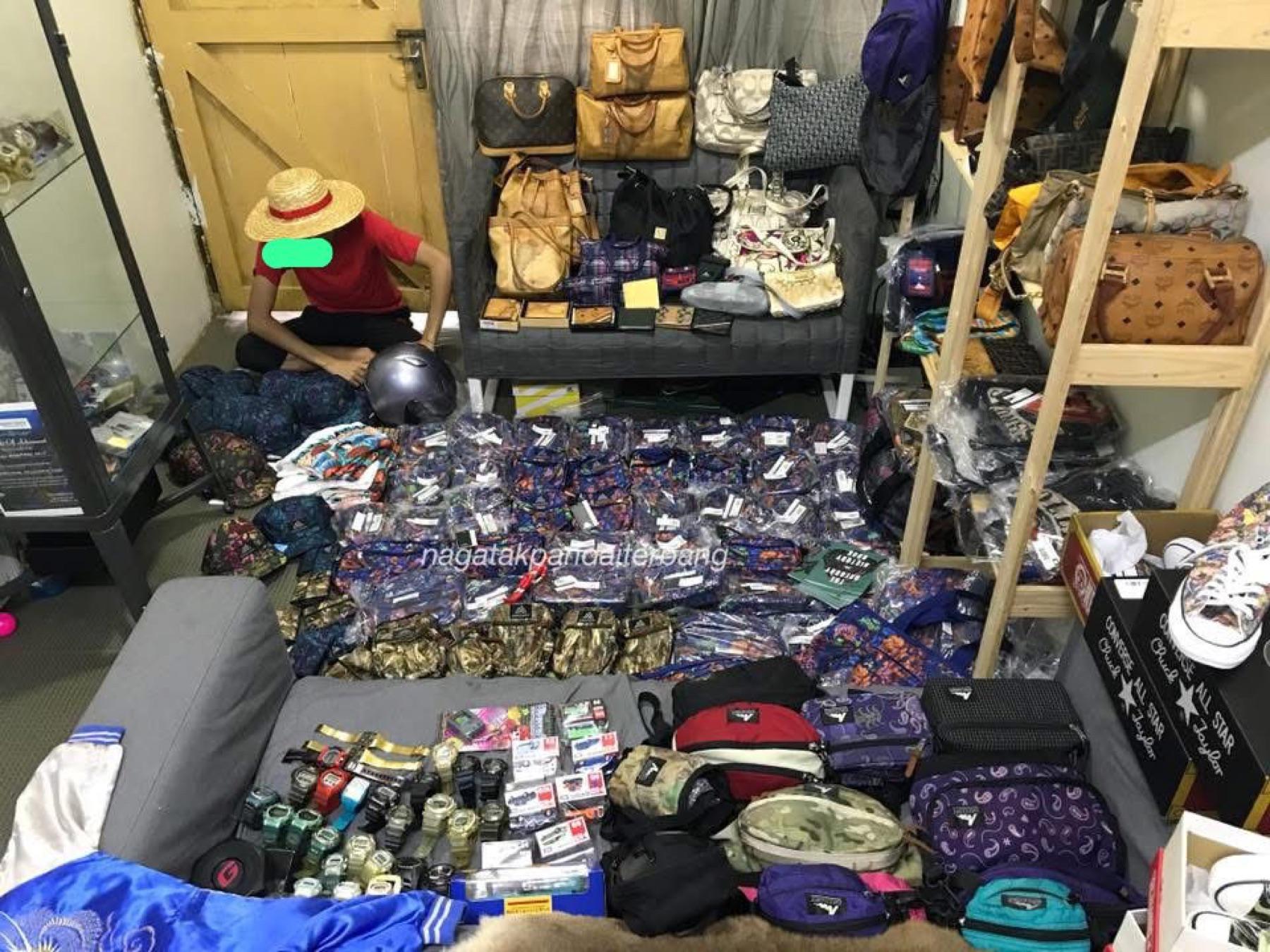 Person in a straw hat sorting sealed bags on the floor of a shop with luxury bags on shelves and Converse boxes