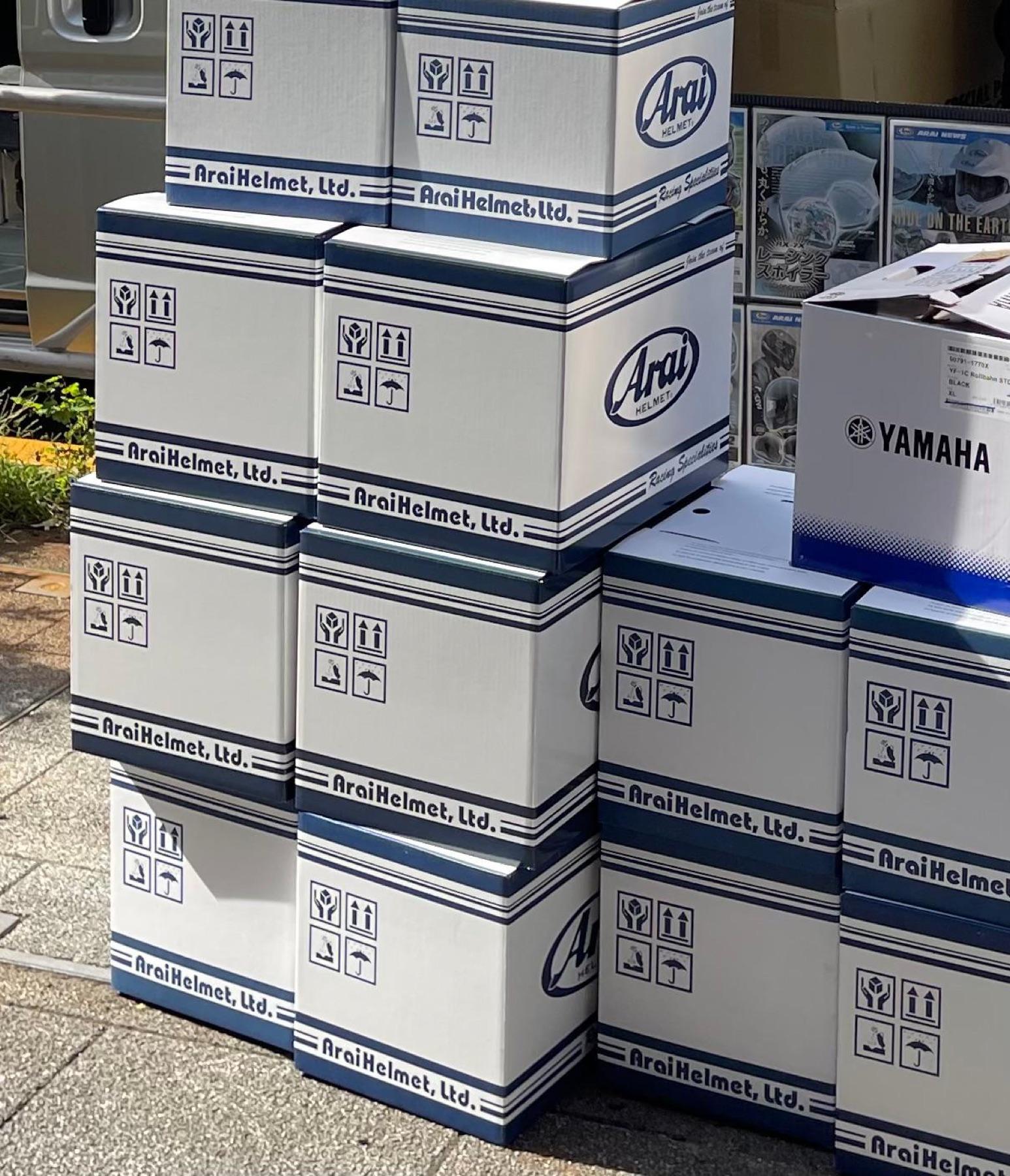 Stack of sealed Arai Helmet cardboard boxes and a Yamaha box outside a shop