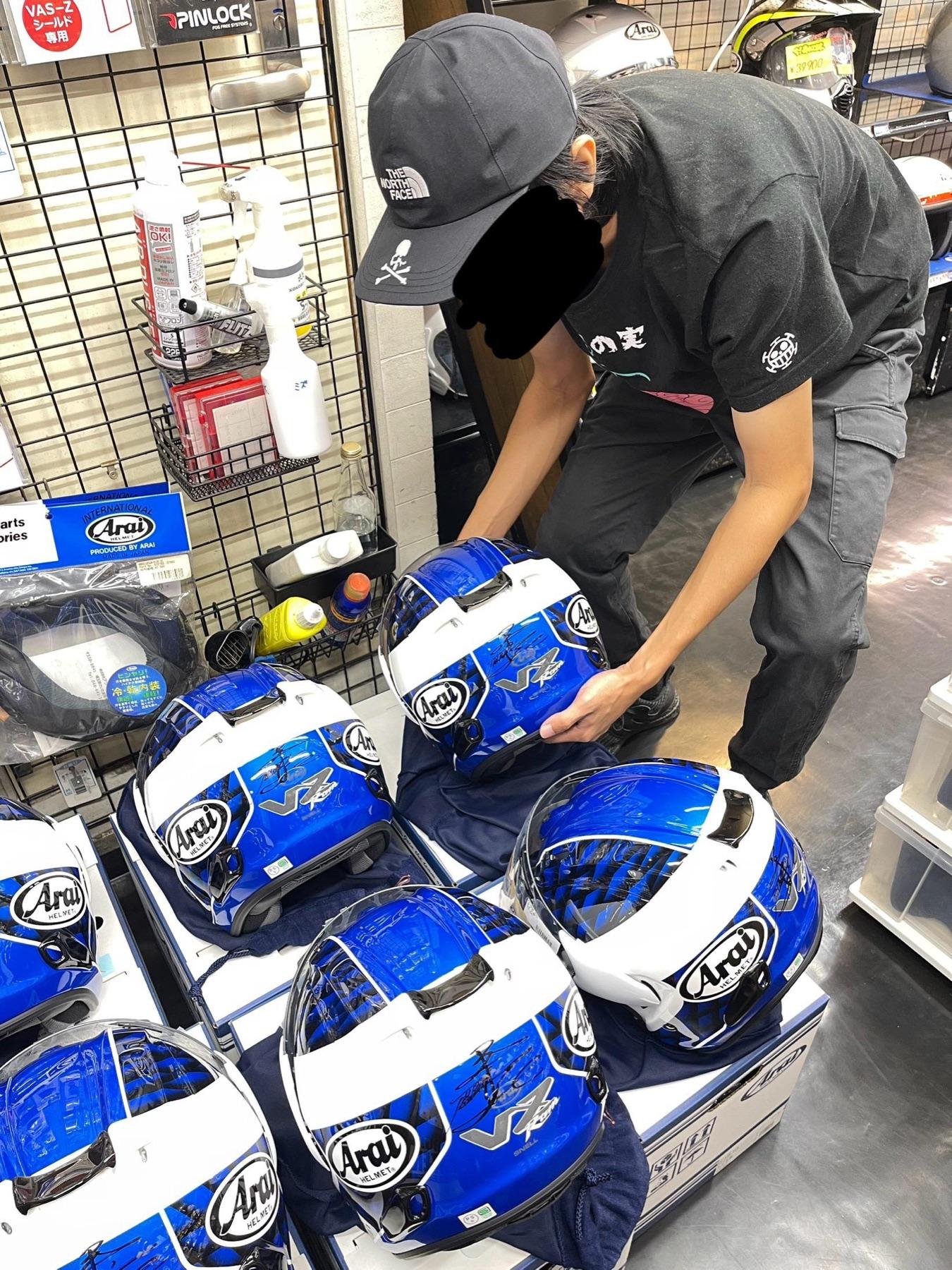 Person in a Japanese helmet shop arranging six blue Arai VZ-Ram helmets, each signed