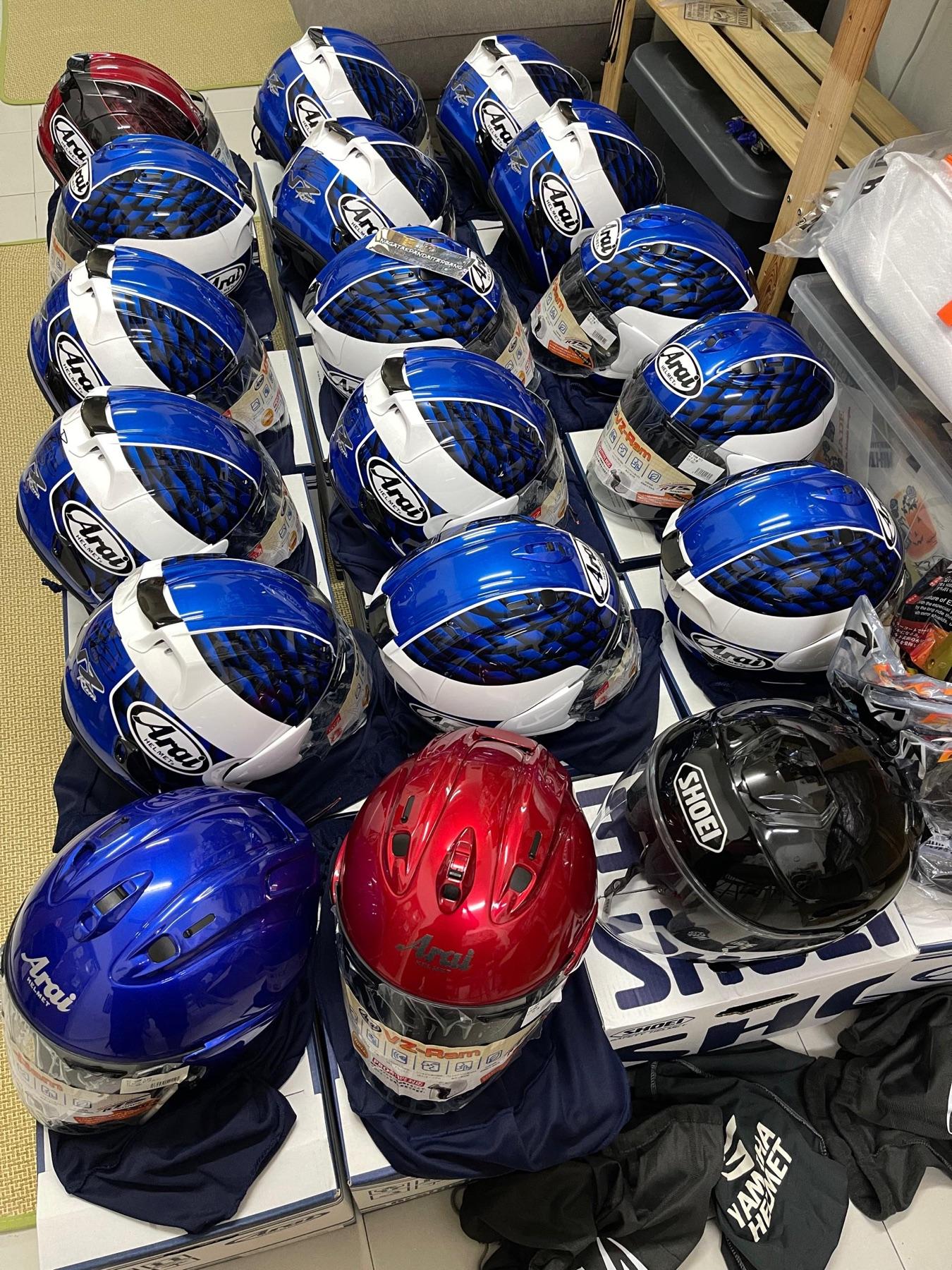 Sixteen blue and white Arai VZ-Ram helmets on their boxes with a Shoei and two solid colour Arai helmets