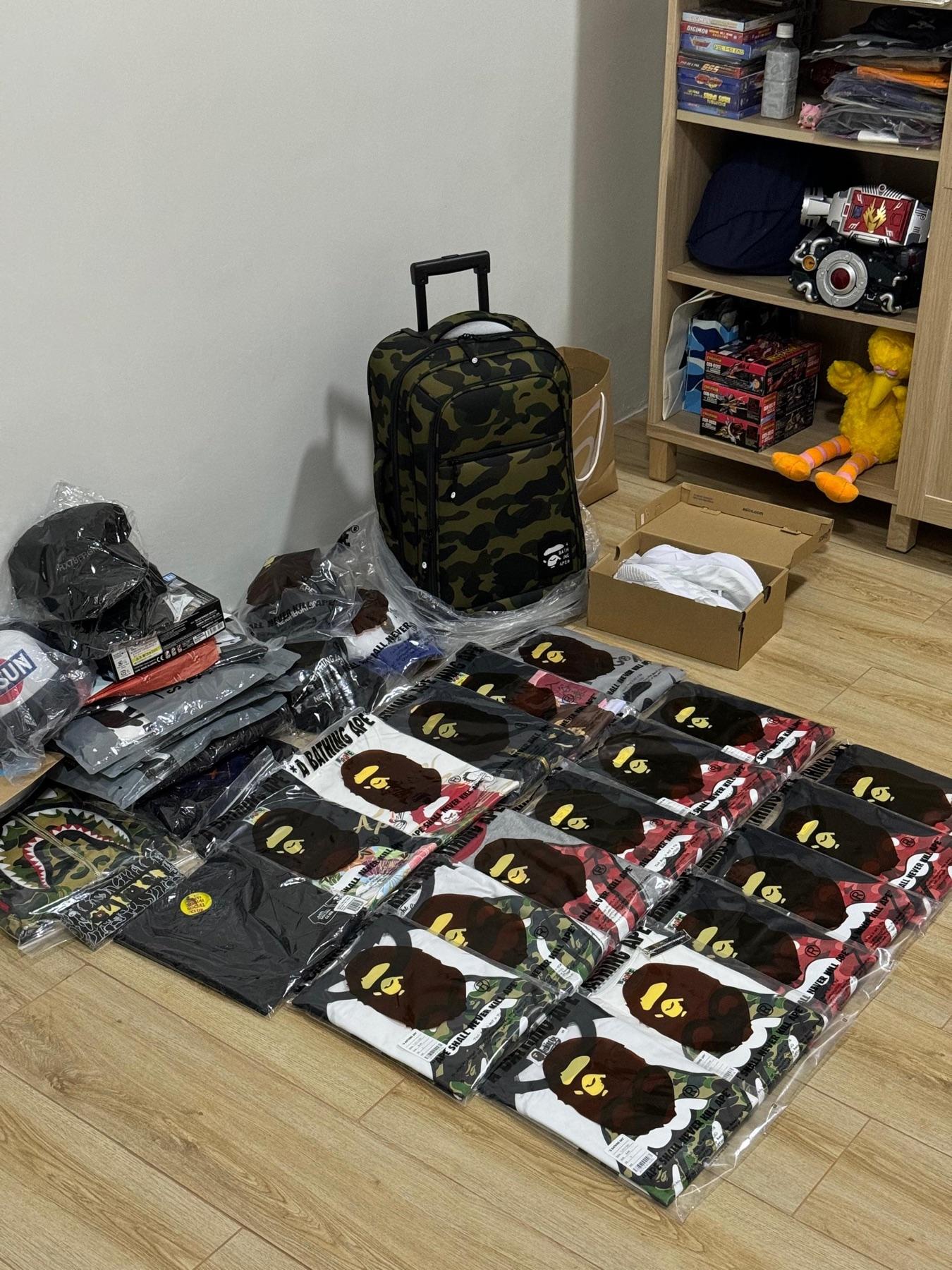BAPE green camo trolley luggage surrounded by rows of sealed BAPE tees in red, green and black camo